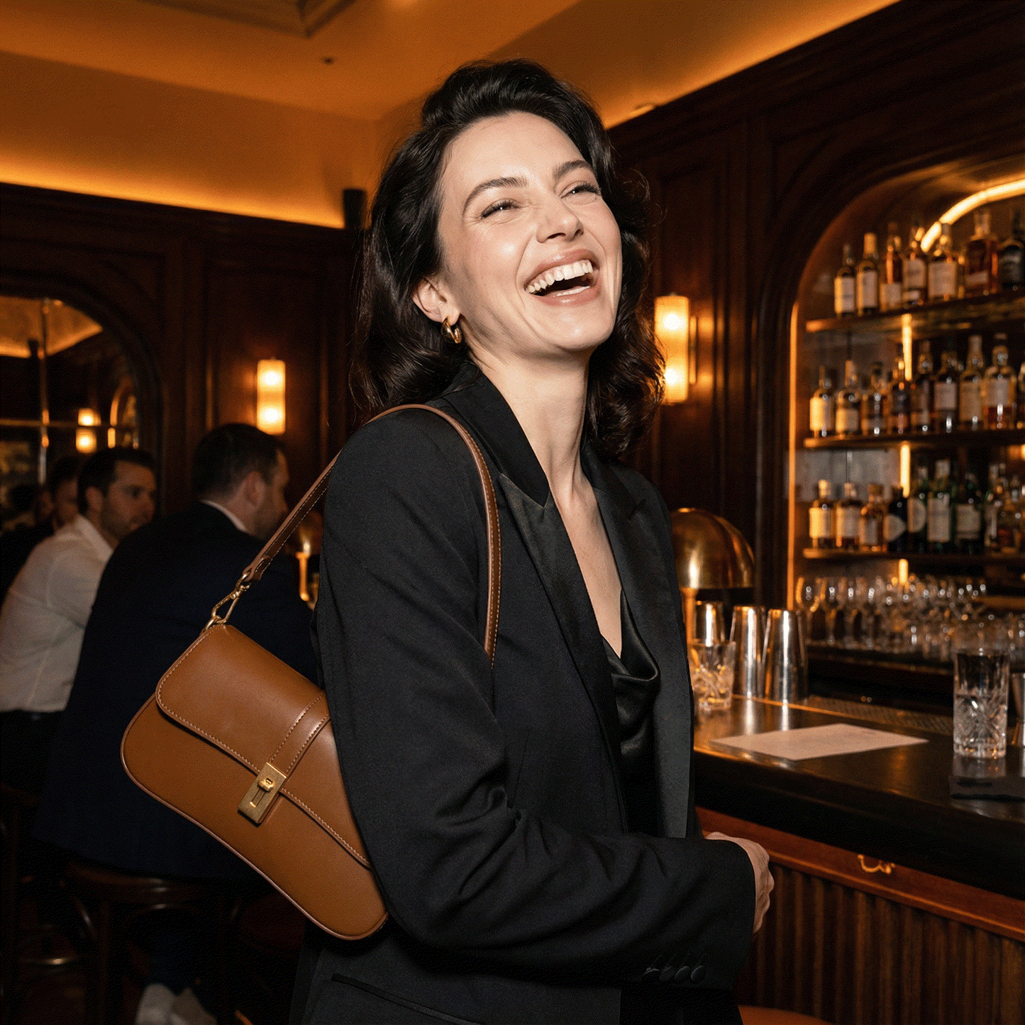 Woman laughing in a bar setting with a brown handbag