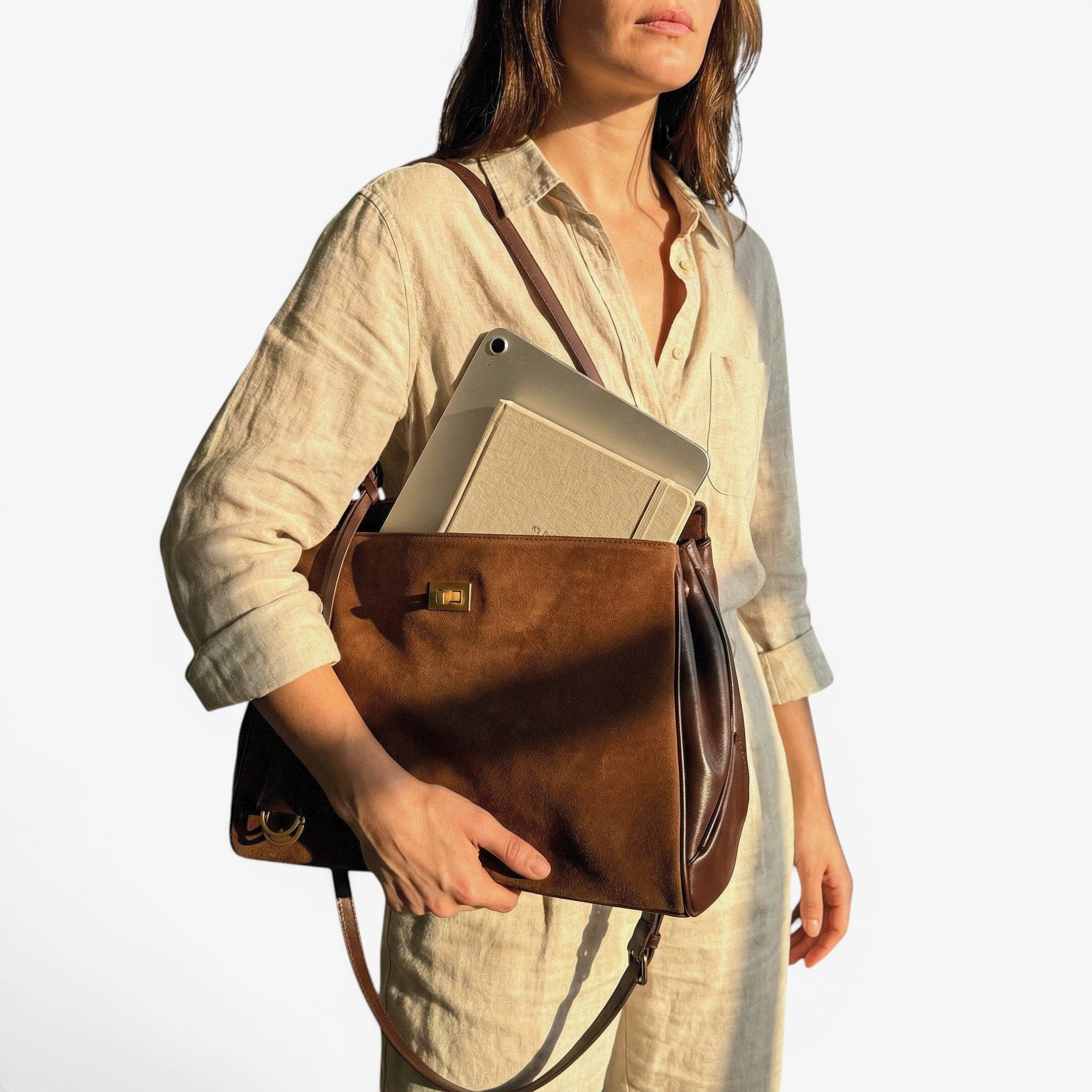 Woman holding a brown leather bag with a laptop inside in a softly lit room.