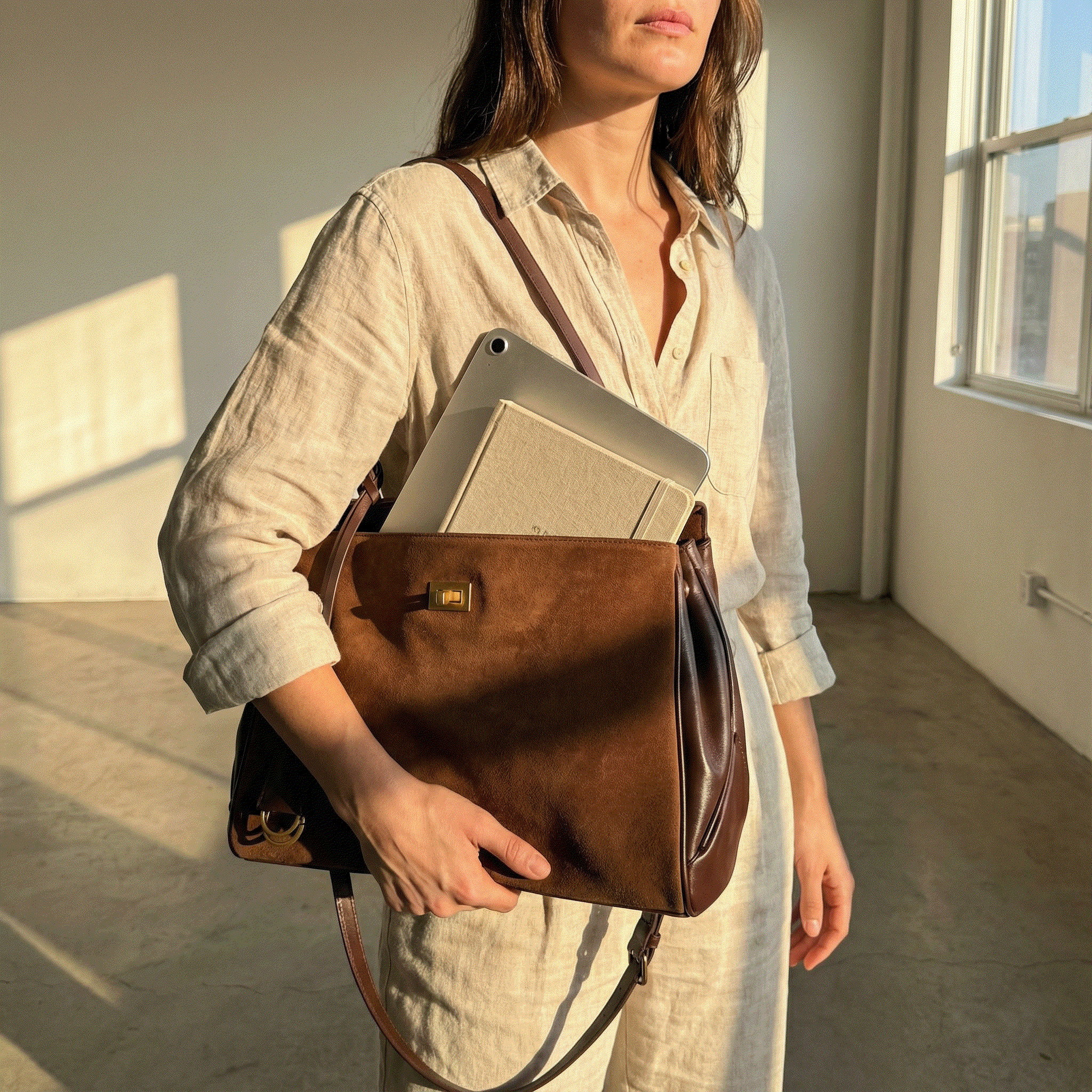 Woman holding a brown leather bag with a laptop inside in a softly lit room.
