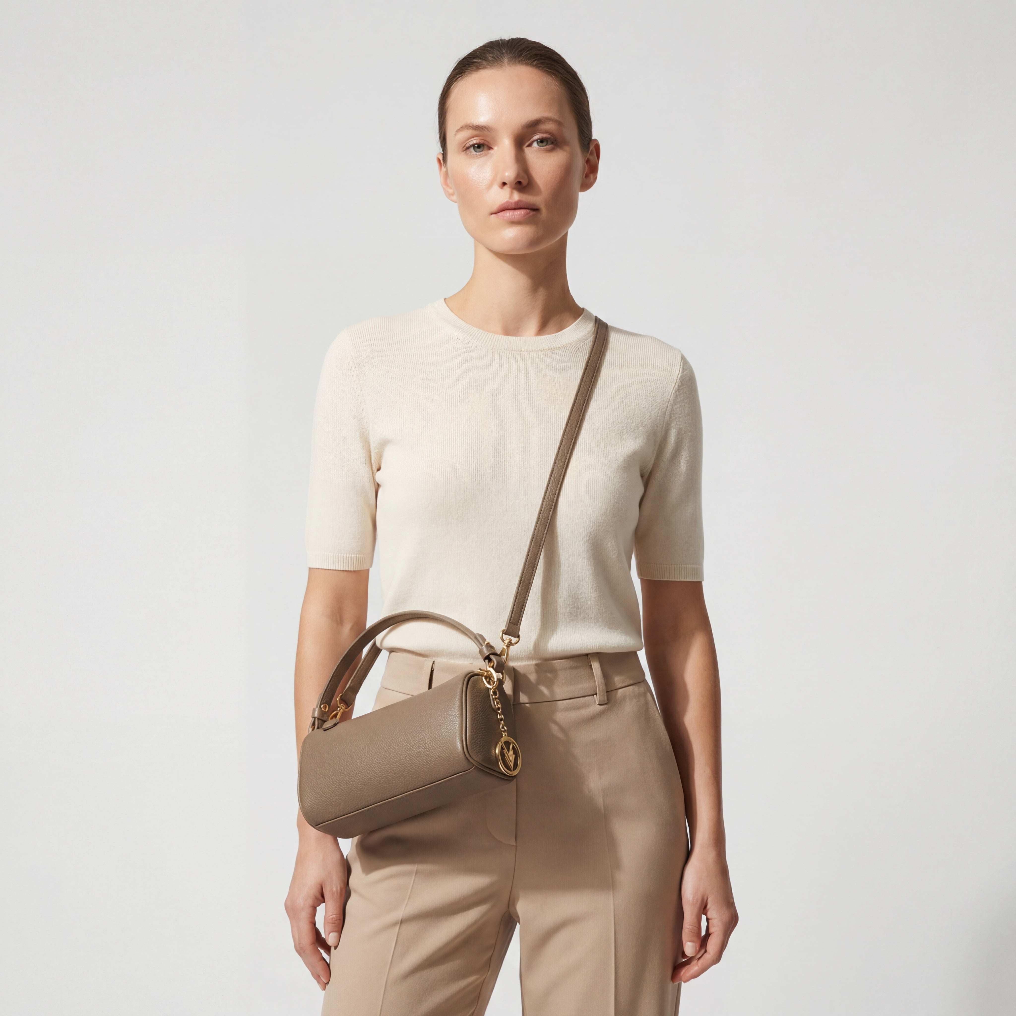 Woman holding a beige handbag against a plain background