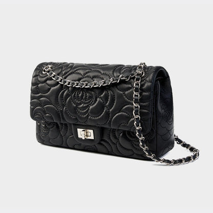 Black quilted handbag with floral design and chain strap on a light gray background