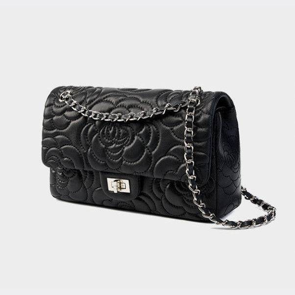 Black quilted handbag with floral design and chain strap on a light gray background