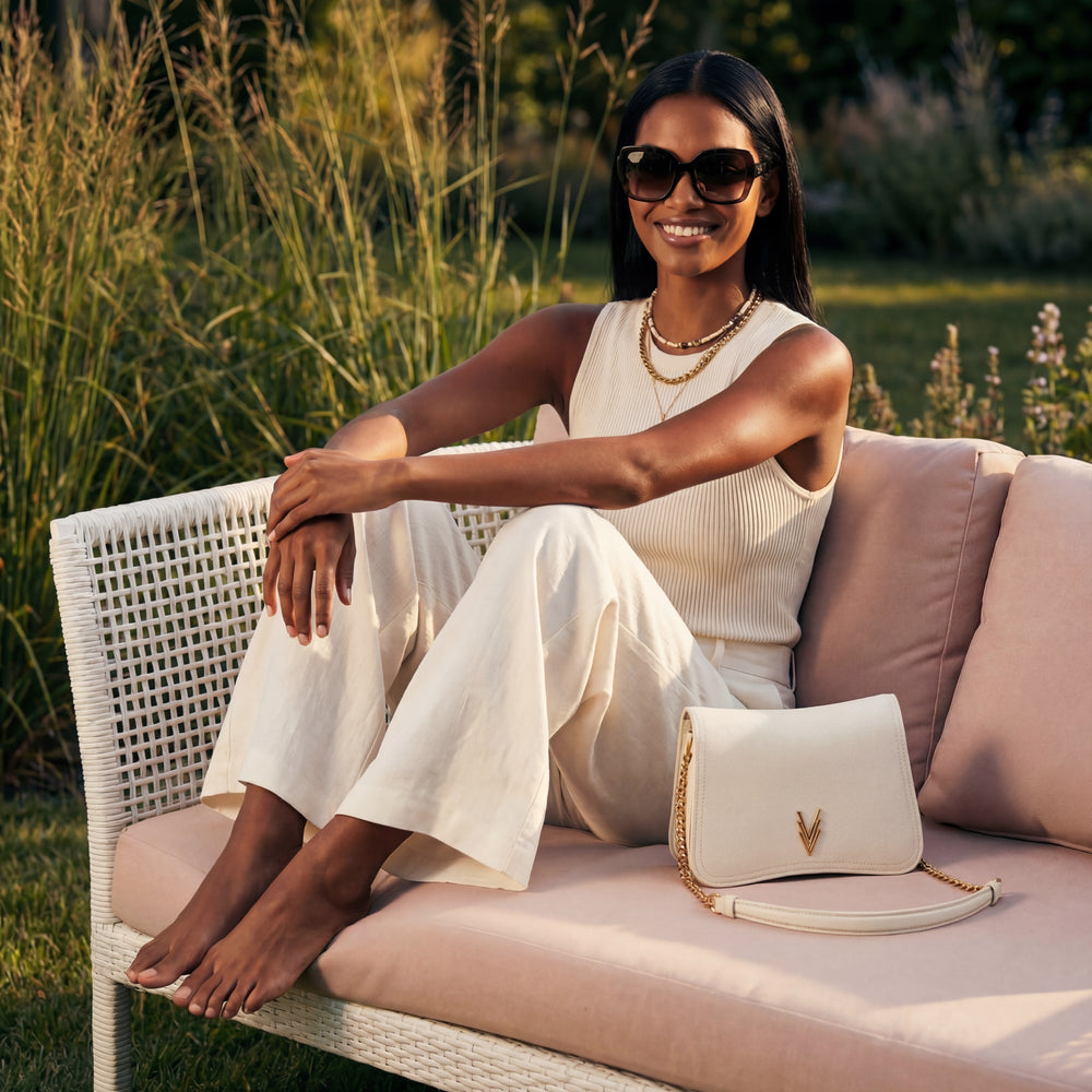 Woman in a white outfit sitting on a pink couch with a white handbag, surrounded by greenery.